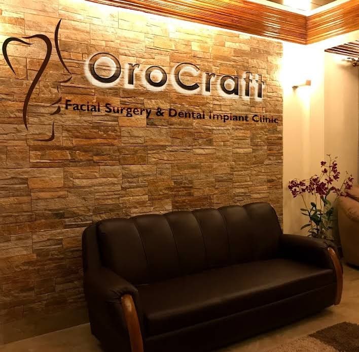 Waiting area of OroCraft clinic with a brown leather sofa and a textured stone wall.