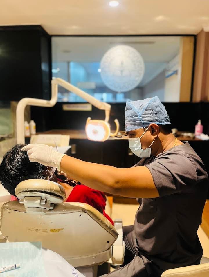 Dentist in scrubs and mask performs a dental procedure on a patient in a clinic.