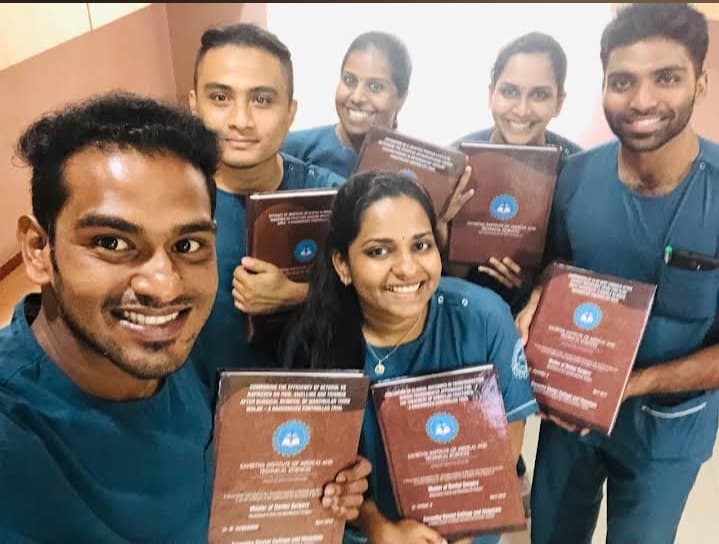 Six smiling medical students in blue scrubs proudly display their brown graduation certificates together.