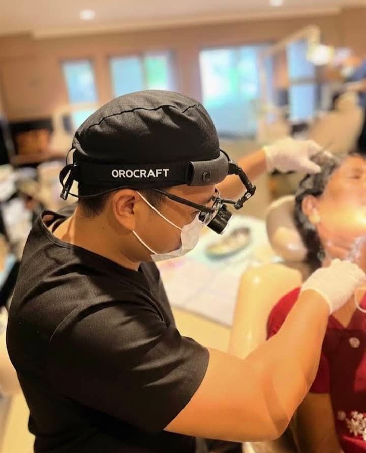 Dentist wearing black scrubs and magnifying loupes performs a dental procedure on a patient.