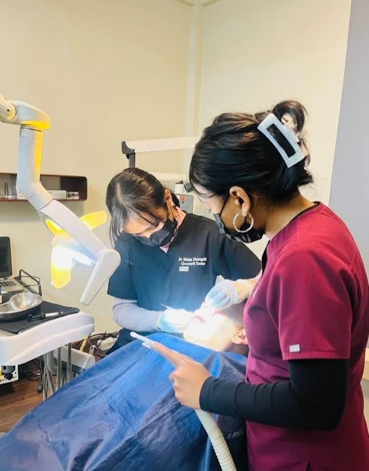 Dentist and assistant in scrubs perform a procedure on a patient under bright light.