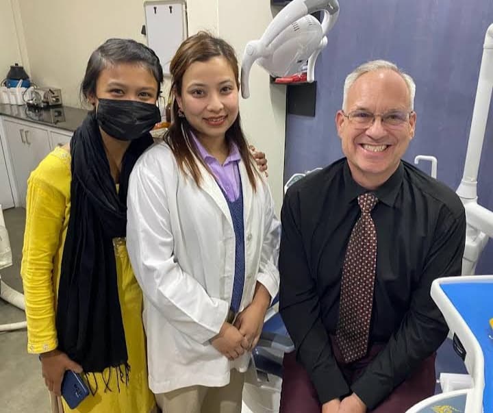 Smiling man in a dental chair with a dentist and a woman in yellow.